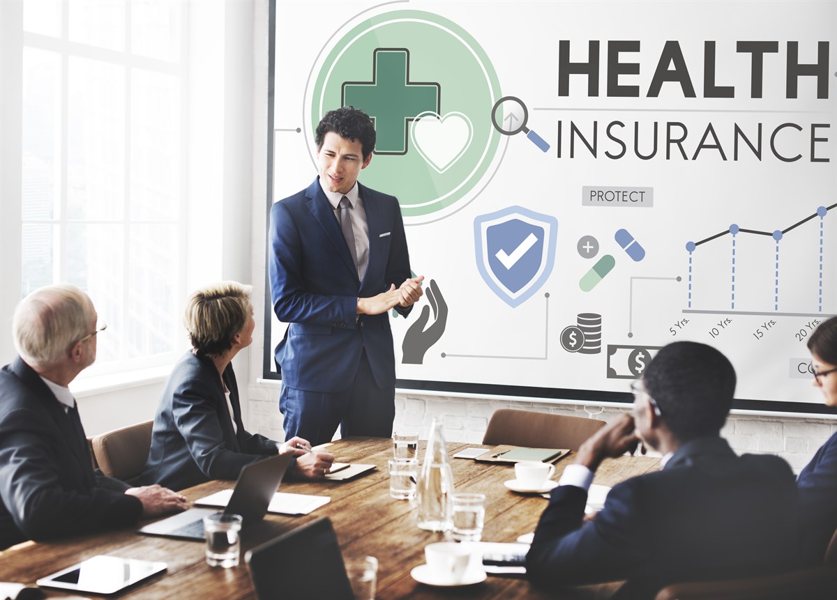 Presenter explaining health insurance coverage to colleagues around a conference table